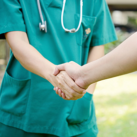 two healthcare professionals in green scrubs shaking hands