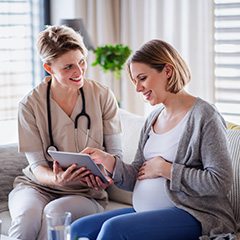 a midwife sitting with a pregnant lady and holding a tablet out to her