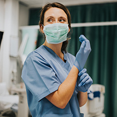 a masked nurse pulling on rubber gloves in an operating theatre