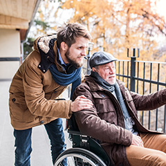 a male carer standing with an elderly man in a wheelchair on a balcony