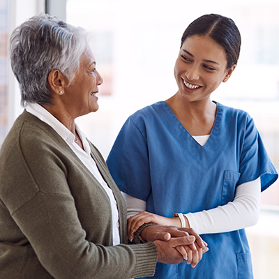 a carer holding the arm of an elderly lady in front of a large window