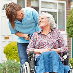 a carer wheeling an elderly lady down a front garden with them smiling at one another