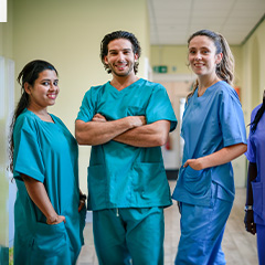 three nurses smiling together at a camera in a hospital corridor