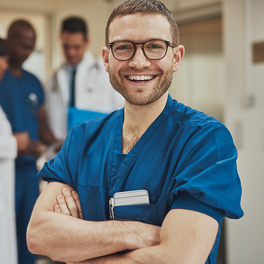 a male nurse posing and smiling at the camera with doctors and a nurse in the background