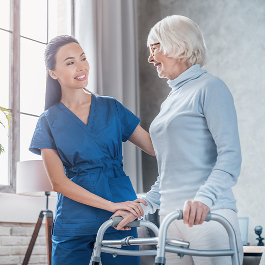 a female nurse helping an elderly lady with a walking frame in a care home